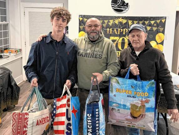 From left, Stone Herbison; Peter Litchfield, commander of Veterans of Foreign Wars Post #7248 in Sparta; and Terry Morris hold donated items collected in the Herbison brothers’ fifth annual Holiday Huddle. More than 200 hats, gloves, socks and blankets for those in need were accepted by the VFW. (Photo provided)