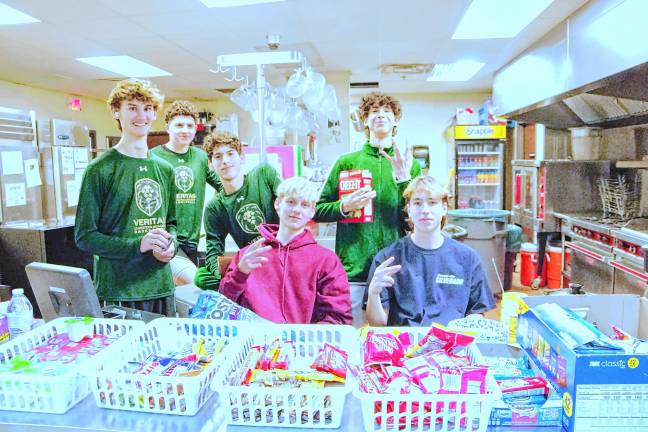 Veritas Christian Academy seniors Lincoln Van Ek, seated left, and Dax Lewicki, seated right, man the snack table. Standing behind them are basketball players. Money from snack purchases helps fund the senior class trip to Cape May later in the year. (Photo by George Leroy Hunter)